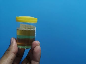 Close-up of person holding glass against blue background
