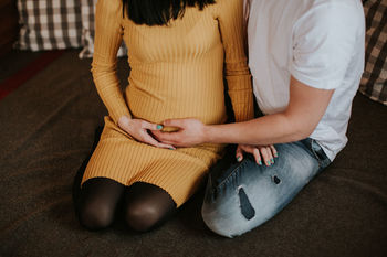MIDSECTION OF WOMAN HOLDING HANDS WHILE SITTING ON TABLE