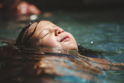 Close-up of girl with eyes closed swimming in pool during sunny day