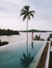 Woman standing by swimming pool against sky