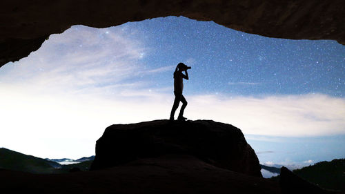 Low angle view of silhouette woman standing on rock against sky