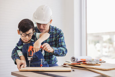 Father assisting son in using drill