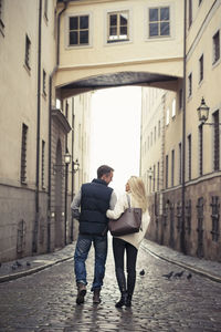 Rear view of couple walking on sidewalk in city