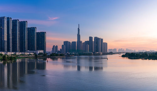 Landmark 81 and other apartment buildings by river against sky during sunset in ho chi minh city