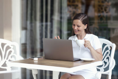 Young woman using phone while sitting on table