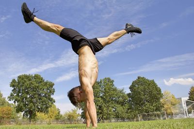 Shirtless man doing handstand on field against sky