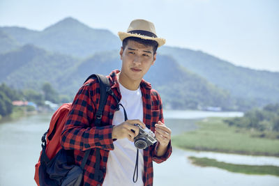 Portrait of young man photographing against mountains