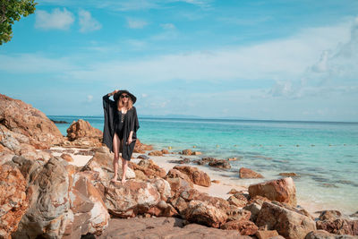 Man standing on rocks by sea against sky