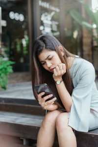 Beautiful young woman using mobile phone while sitting outdoors