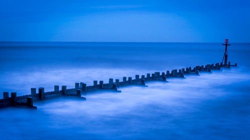 Wooden posts in sea against blue sky