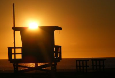 Silhouette lifeguard hut at beach against orange sky during sunset