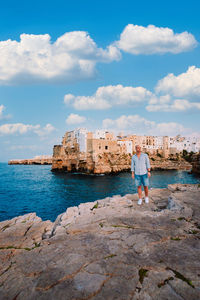 Man standing on the rocks in front of the village of polignano a mare