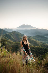A blond woman is enjoying the beautiful view of mt. agung and the green surrounding.