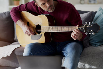 Midsection of man playing guitar on sofa at home