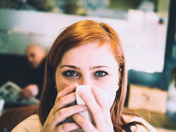 Close-up portrait of young woman drinking coffee in cafe