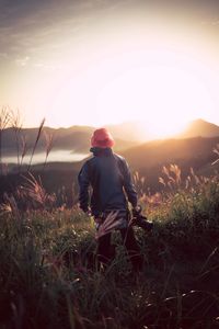 Rear view of man standing on field against sky during sunset