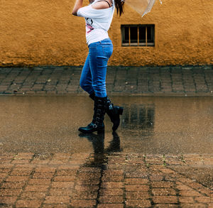 Low section of woman walking on wet street during rainy season