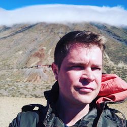Man looking away by volcanic mountains against cloudy sky