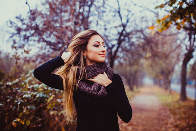 Beautiful young woman standing against trees during autumn