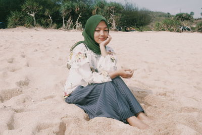 Beautiful young woman sitting on sand at beach