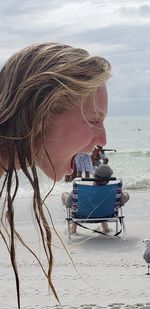 Woman sitting on beach by sea against sky