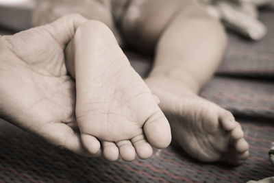 Cropped hand holding baby feet on bed