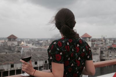 Rear view of woman holding wine glass against cityscape