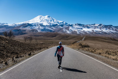 Rear view of man walking on road against mountain