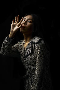 Portrait of young woman looking away against black background