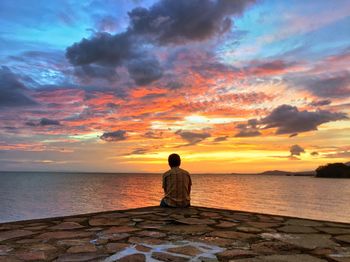 Silhouette man sitting on beach against sky during sunset