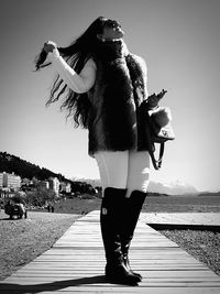 Woman standing on footpath by sea against sky