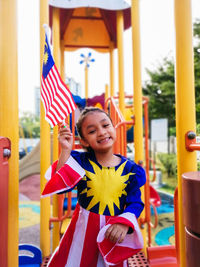 Portrait of smiling girl holding malaysian flag on jungle gym at playground