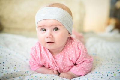 Portrait of cute baby girl lying on bed at home