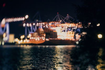 Illuminated city by river against sky at night