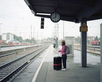 Side view of woman with luggage standing on railroad station