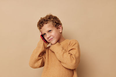 Boy talking on phone against beige background
