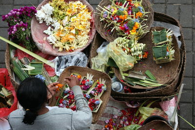 High angle view of female vendor making flower garlands on street market