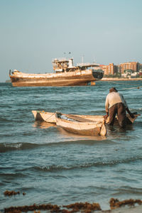 A fisherman pushing his boat in sea against clear sky