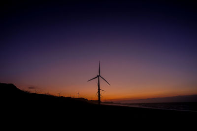 Silhouette wind turbines on land against sky during sunset