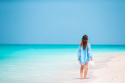 Boy standing on beach against clear blue sky