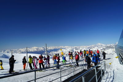People skiing against snowcapped mountain and clear blue sky