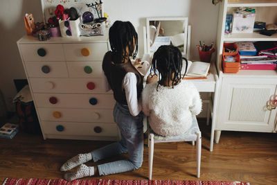 Girl kneeling by sister doing homework at home