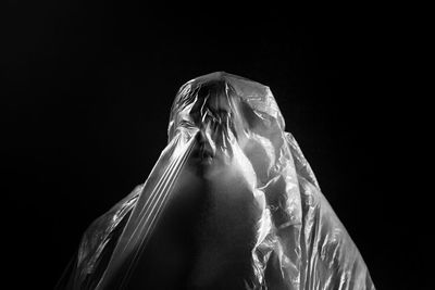 Person wrapped in plastic against black background