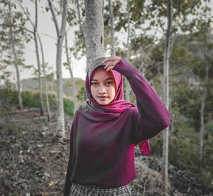 Portrait of young woman standing by tree in forest