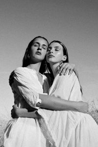 Lesbian couple with eyes closed embracing against sky