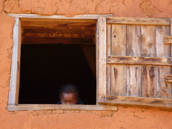 Portrait of boy looking through old window of house