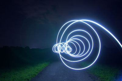 Light trails on road amidst field against sky at night