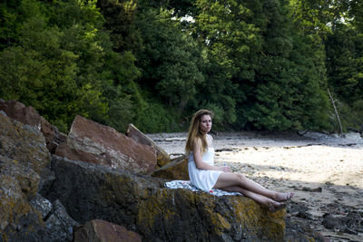 Portrait of young woman sitting on rock against trees