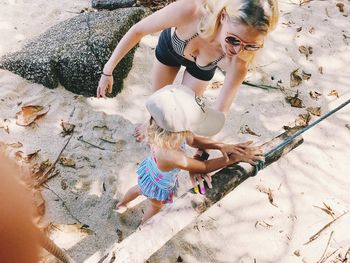 High angle view of mother and daughter touching wood at beach