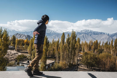 Side view of man standing on retaining wall while looking at view during winter